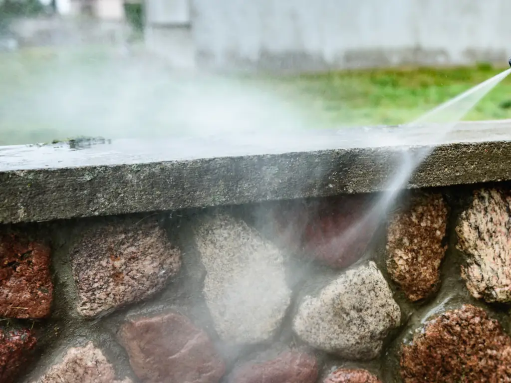A power washing stream cleans an outdoor stone wall during exterior property cleaning in South Jersey.