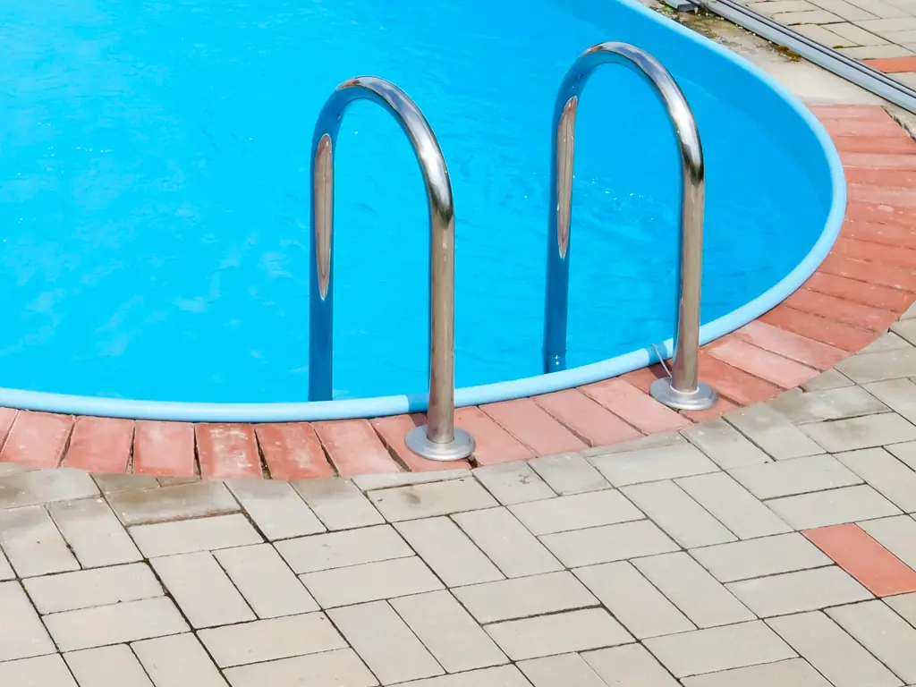 Clean inground pool handrails and steps on a paver patio in Collingswood, NJ after professional pressure washing — removing algae and calcium deposits from pool surrounds.